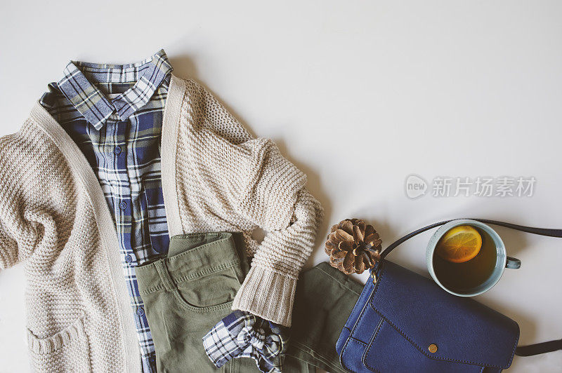 秋女人休闲时尚set flat lay with copy space。格子衬衫，针织毛衣，蓝色斜挎包和卡其布裤子在白色背景。时髦的服装俯视图。